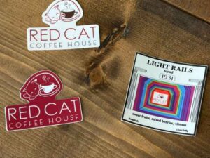 Photograph of all 3 stickers: A white background with red Red Cat logo; a red background with a white Red Cat logo; a sticker version of the Light Rails coffee logo